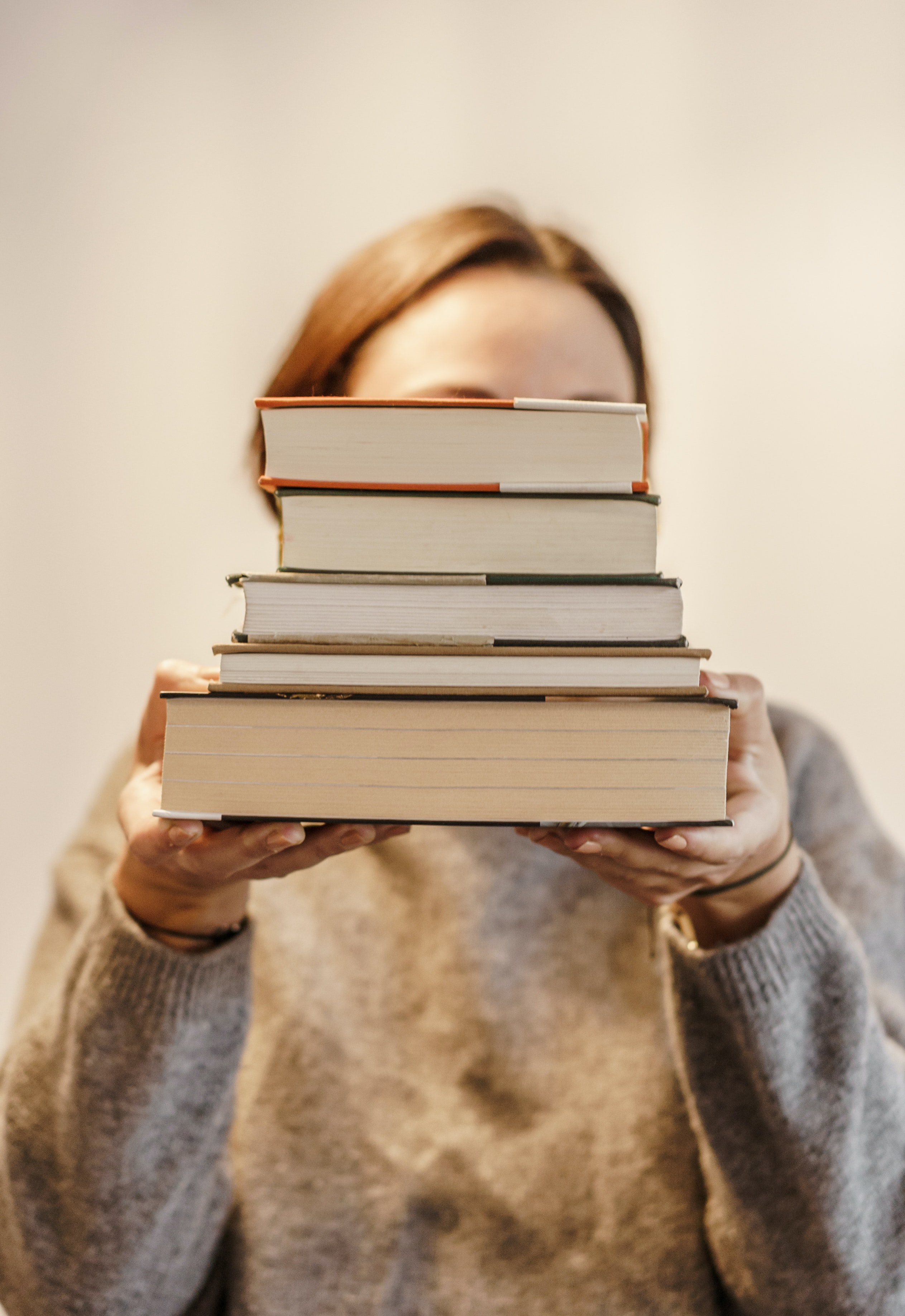 A woman holding a pile of books in front of her face
